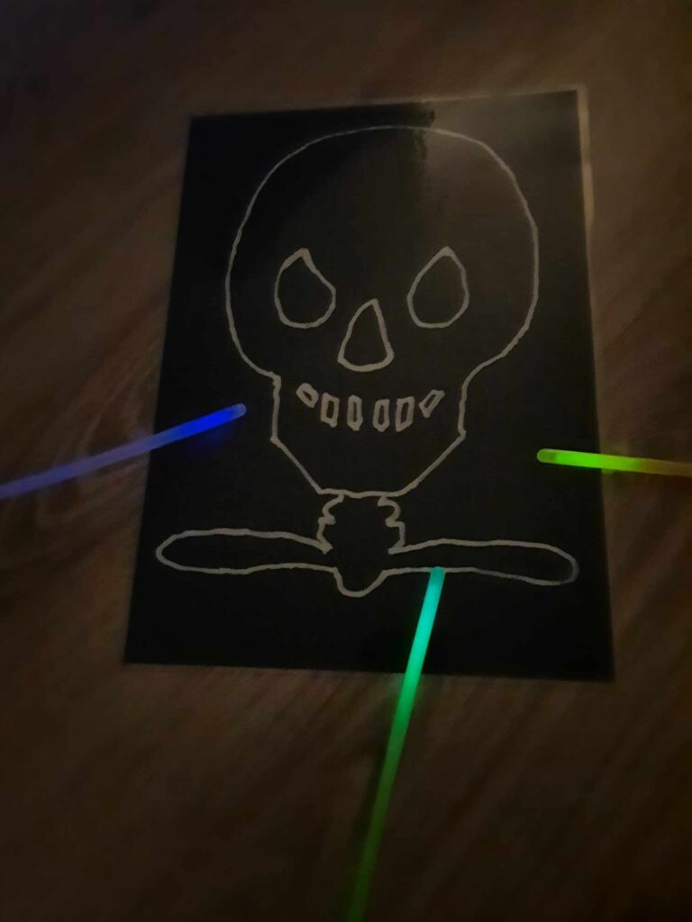 czaszka na czarnym tle ze świecącymi patyczkami fluorescencyjnymi - fiszki DIY na halloween